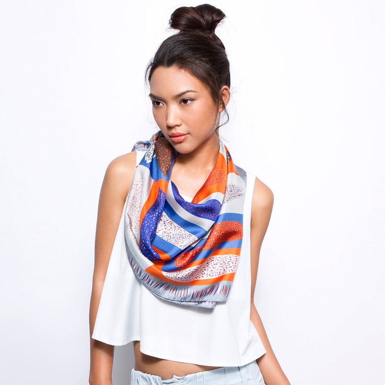 May include: A woman wearing a white sleeveless top and a colourful patterned scarf. The scarf is blue, orange, and white with a geometric design.