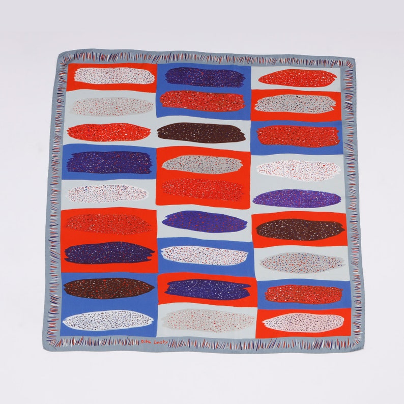 May include: A blue and white silk scarf with a repeating pattern of colourful brushstrokes. The scarf has a fringed edge and the text "Silk Lovely" is printed in the bottom right corner.