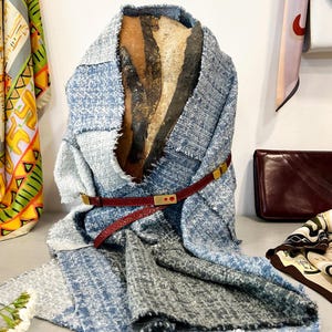May include: A blue and grey patchwork scarf with a red leather belt and gold buckle. The scarf is folded and draped over a textured surface.