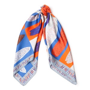 May include: A blue, orange and white patterned silk scarf with a geometric design. The scarf is tied in a knot and the ends are hanging down.