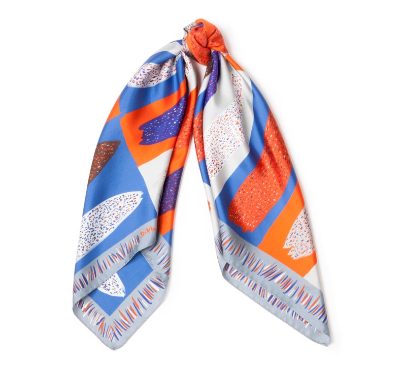 May include: A blue, orange and white patterned silk scarf with a geometric design. The scarf is tied in a knot and the ends are hanging down.