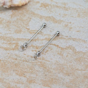 May include: Two silver earring components. Each component features a straight bar with a small ball at one end and a loop at the other. They are displayed on a light-coloured, textured surface.