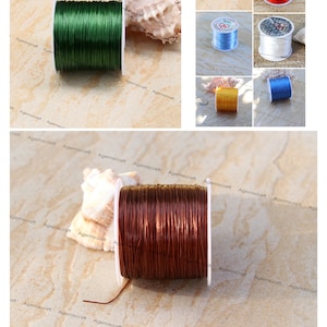 May include: A selection of elastic beading cord spools in colours such as green, red, blue, white, yellow, and brown. The cord is wound on white spools, ideal for jewellery making and crafts. A seashell is also present in the image.