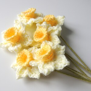 May include: A bouquet of crocheted daffodils with yellow centers and white petals. The flowers are attached to green stems.