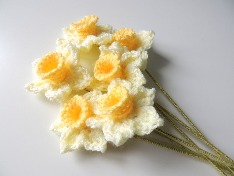 May include: A bouquet of crocheted daffodils with yellow centers and white petals. The flowers are attached to green stems.
