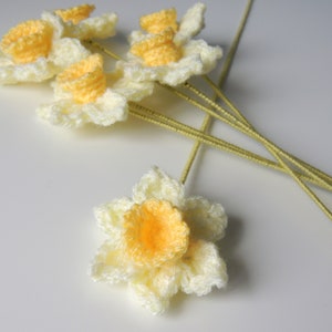 May include: A bunch of crocheted daffodils with yellow centers and white petals. The flowers are attached to green stems.