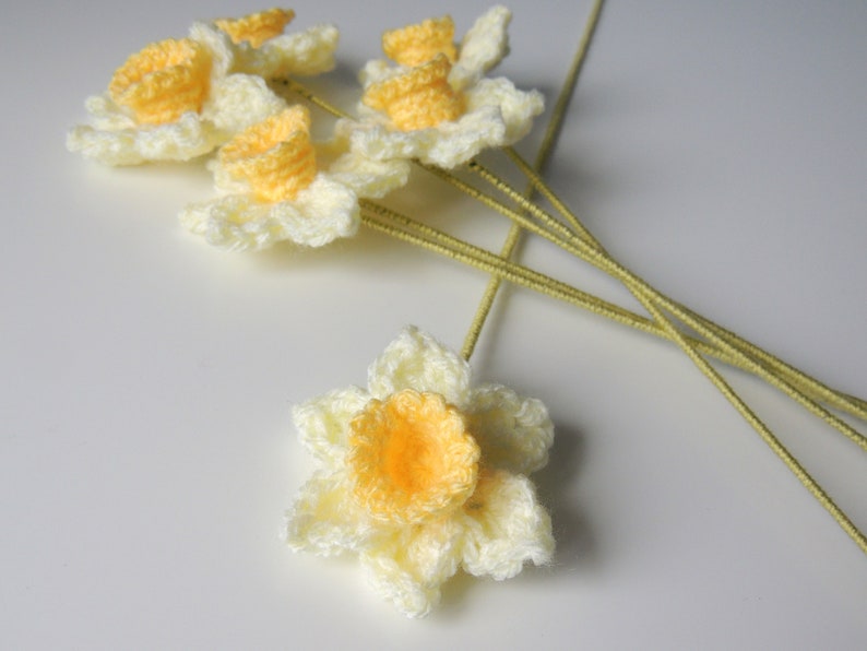 May include: A bunch of crocheted daffodils with yellow centers and white petals. The flowers are attached to green stems.