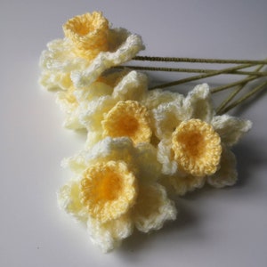 May include: A bunch of crocheted daffodils in shades of yellow and white. The flowers are arranged in a bouquet and have green stems.