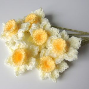 May include: A bunch of crocheted daffodils in cream and yellow with green stems.