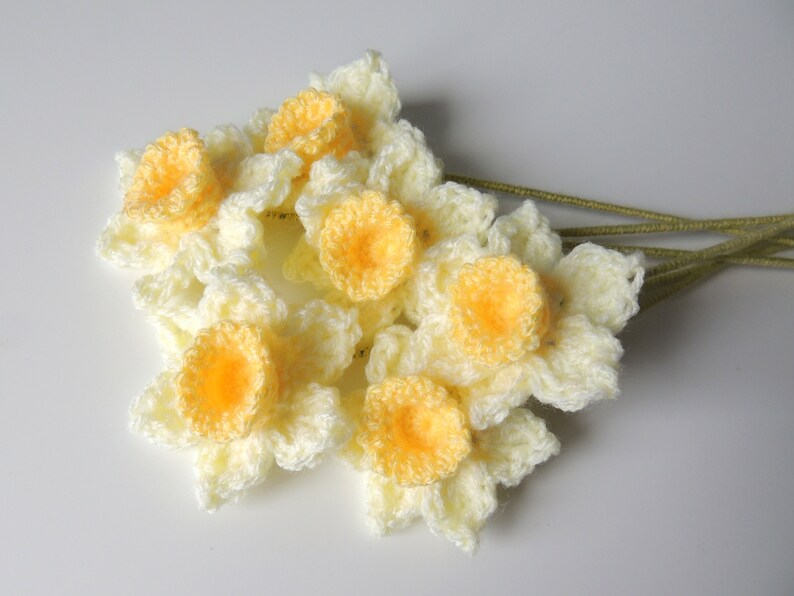 May include: A bunch of crocheted daffodils in cream and yellow with green stems.