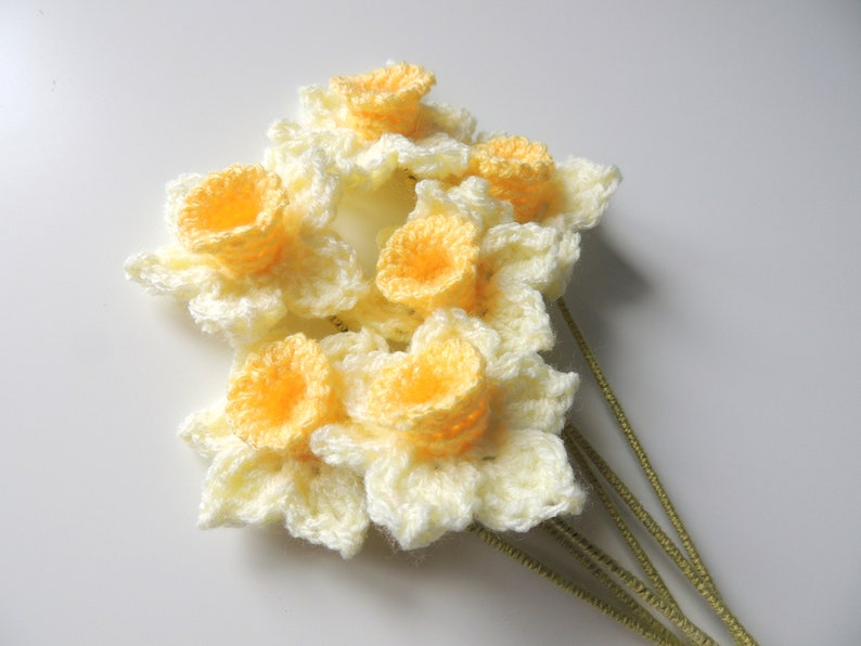 May include: A bunch of crocheted daffodils with yellow centers and white petals. The flowers are attached to green stems.