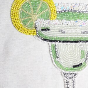 May include: A beaded margarita glass with a lime wedge, made with green, white, and silver beads.