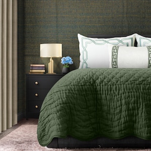 Op de afbeelding: Een groene gestikte bedsprei met een wit kussen met een groen geometrisch patroon. De bedsprei ligt op een bed met een donkergroene hoofdeinde.