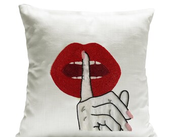 May include: White pillow with a red beaded lips design and a black outlined finger over the lips, symbolizing silence.