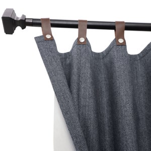 Pode incluir: Cortinas com padrão de espinha de peixe cinza e branco com abas de couro marrom penduradas em uma haste de cortina preta com um acabamento decorativo.