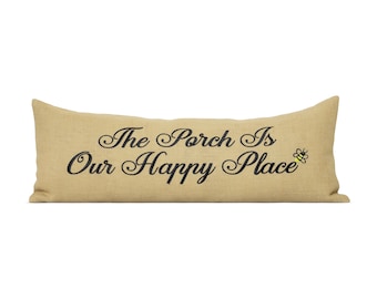 Könnte beinhalten: Ein langes, rechteckiges Kissen aus beigem Jute mit dem gestickten Text "The Porch Is Our Happy Place" in schwarzer Schrift. Eine kleine gelb-schwarze Bienen-Grafik befindet sich auf der rechten Seite des Textes.