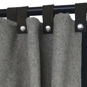 Puede incluir: Cortinas grises con pestañas de cuero negro y anillos de metal plateado colgados de una barra de cortina negra.