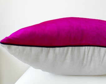Op de afbeelding: Een rechthoekig sierkussen met een fel magenta fluwelen bovenkant en een effen witte onderkant met linnenstructuur. Een dunne, donker marineblauwe bies loopt horizontaal langs de middennaad en scheidt de twee verschillende stoffen van elkaar.