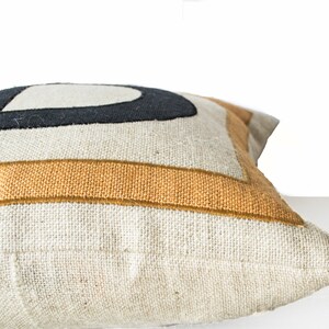 May include: A white linen pillow with a black and mustard yellow geometric design. The pillow is shown from the side, with the seam visible.