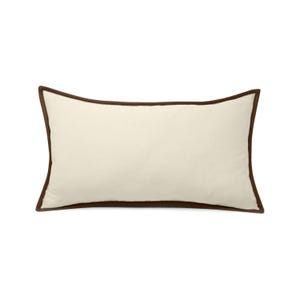 May include: Cream-colored rectangular pillow with a dark brown border. The pillow has a simple, elegant design, suitable for various home decor styles. The pillow's dimensions are approximately 12 inches by 20 inches.