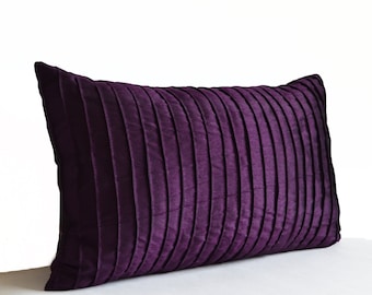 May include: A rectangular throw pillow in a deep, rich purple hue. The surface of the pillow features a series of vertical, evenly spaced pleats that run across the entire length, creating a textured, dimensional appearance with a subtle sheen.
