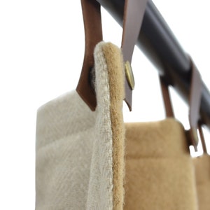 Puede incluir: Dos cortinas de tela con un lazo de colgar de cuero marrón y un botón de latón. Las cortinas son beige y marrón.