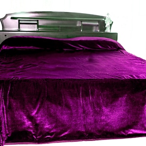 May include: A bed with a dark wooden headboard and a deep purple velvet bedspread. The headboard has a built-in shelf and a small decorative figurine. The bed is against a white background.
