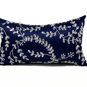 May include: A navy blue pillow with a white floral embroidery design. The pillow is rectangular and has a soft, plush texture.