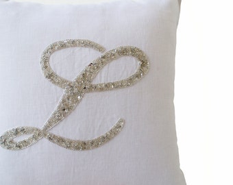 May include: White pillow with a large letter L made of silver sequins.