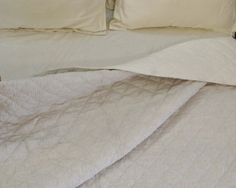 May include: A white quilted bedspread with a subtle pattern, folded back to reveal a white sheet and two white pillows.