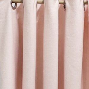 Puede incluir: Un juego de cinco cortinas de color rosa claro con ojales plateados colgados de una barra de madera.