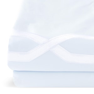 Op de afbeelding: Een stapel gevouwen witte lakens met een lichtblauwe tint. Witte elastische banden kruisen elkaar over het bovenste laken, wat een decoratief element toevoegt. De lakens zien er zacht en glad uit.