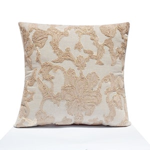 Può includere: Cuscino quadrato decorativo con sfondo color crema e motivo floreale ricamato in beige chiaro. Il cuscino ha un aspetto morbido e strutturato, e il motivo floreale è dettagliato e complesso. Adatto per l'arredamento della casa.