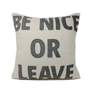 May include: Square decorative pillow with the text "BE NICE OR LEAVE" in dark gray letters. The pillow has a textured, off-white background. The letters are sewn onto the pillow.