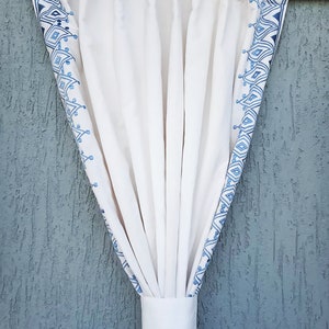 Può includere: Tende bianche con un motivo geometrico blu sui bordi. Le tende sono legate con un laccio in tessuto bianco.