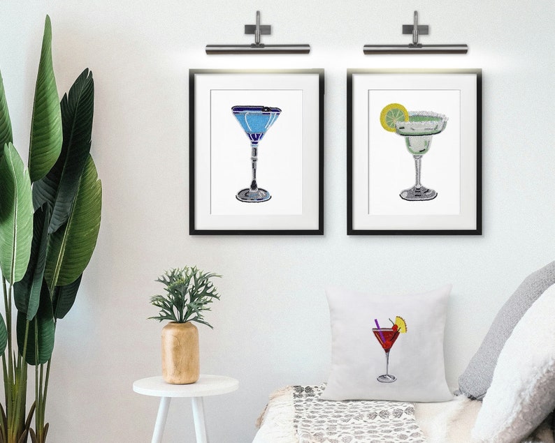 May include: Three framed illustrations of cocktails. The first is a blue martini, the second is a green margarita with a lime wedge, and the third is a red cosmopolitan with a lime wedge and a cherry.