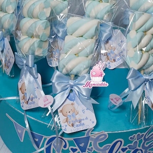 Può includere: Marshmallow su bastoncini, avvolti in cellophane trasparente e legati con fiocchi azzurri. Ogni dolcetto ha un'etichetta con l'illustrazione di un orsetto e il testo "Il Battesimo di Giulio 6 luglio 2025".