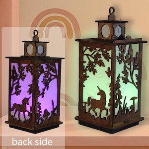 Puede incluir: Dos faroles de madera con temática de unicornio. Los faroles tienen forma rectangular con diseños recortados de árboles, setas y un unicornio. Los faroles están iluminados con luces moradas y verdes.