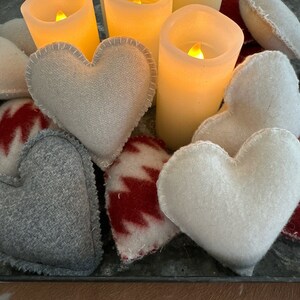 Puede incluir: Una bandeja con velas encendidas y almohadas en forma de corazón de fieltro blanco. La bandeja está decorada con tela estampada roja y blanca.