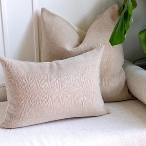 May include: Two rectangular throw cushions featuring a woven beige and white herringbone pattern. The cushions are constructed from a textured fabric and display a consistent chevron-like weave throughout the surface of both cushion covers.
