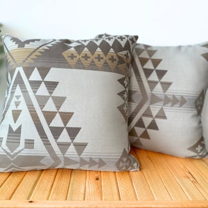 Op de afbeelding: Twee decoratieve kussens met een geometrisch patroon in tinten bruin, beige en wit. De kussens zijn gemaakt van een zachte, textuurrijke stof en hebben een modern ontwerp.