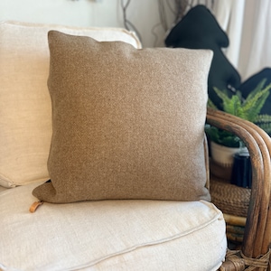 May include: A brown throw pillow with a textured surface sits on a white linen sofa with a woven rattan frame.