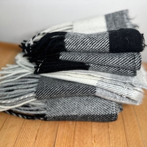 Puede incluir: Una pila de bufandas de cuadros negros y blancos con flecos. Las bufandas están dobladas y apiladas sobre una superficie de madera.