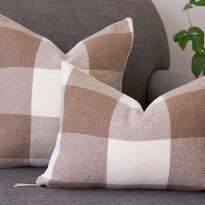 May include: Two brown and white checked throw pillows on a grey sofa. The pillows are made of a soft, woven fabric.