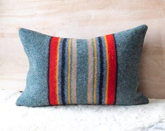 May include: A blue and red striped throw pillow with a wool texture. The pillow is rectangular and has a subtle sheen.