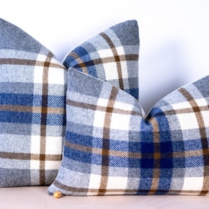 Puede incluir: Tres cojines decorativos con estampado de cuadros azules, blancos y marrones, en diferentes tamaños. Los cojines tienen un aspecto suave y texturizado. El diseño de cuadros es un patrón clásico.