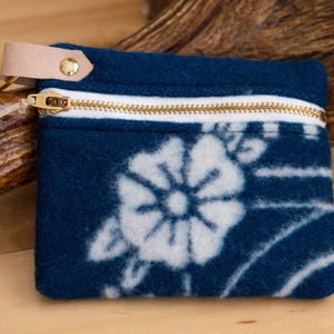 May include: A small blue zippered pouch with a white floral pattern. The pouch has a leather strap with a metal ring.