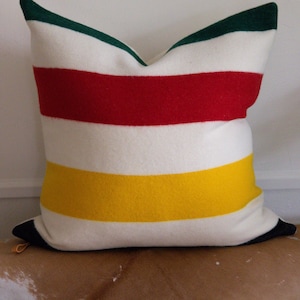 May include: A striped cushion with red, yellow, green and white stripes. The cushion is made of a soft, fuzzy material.