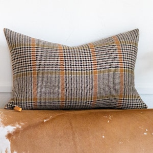 May include: A brown, beige and orange plaid throw pillow with a subtle houndstooth pattern.