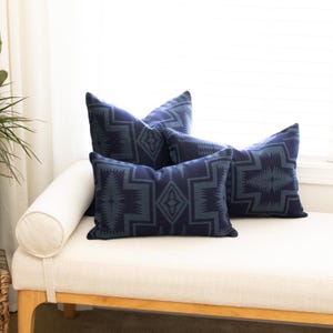 Op de afbeelding: Vier marineblauwe sierkussens met een geometrisch patroon in een lichtere blauwtint. De kussens zijn rechthoekig en op een witte chaise longue geplaatst. De kussens geven de kamer een decoratieve touch.